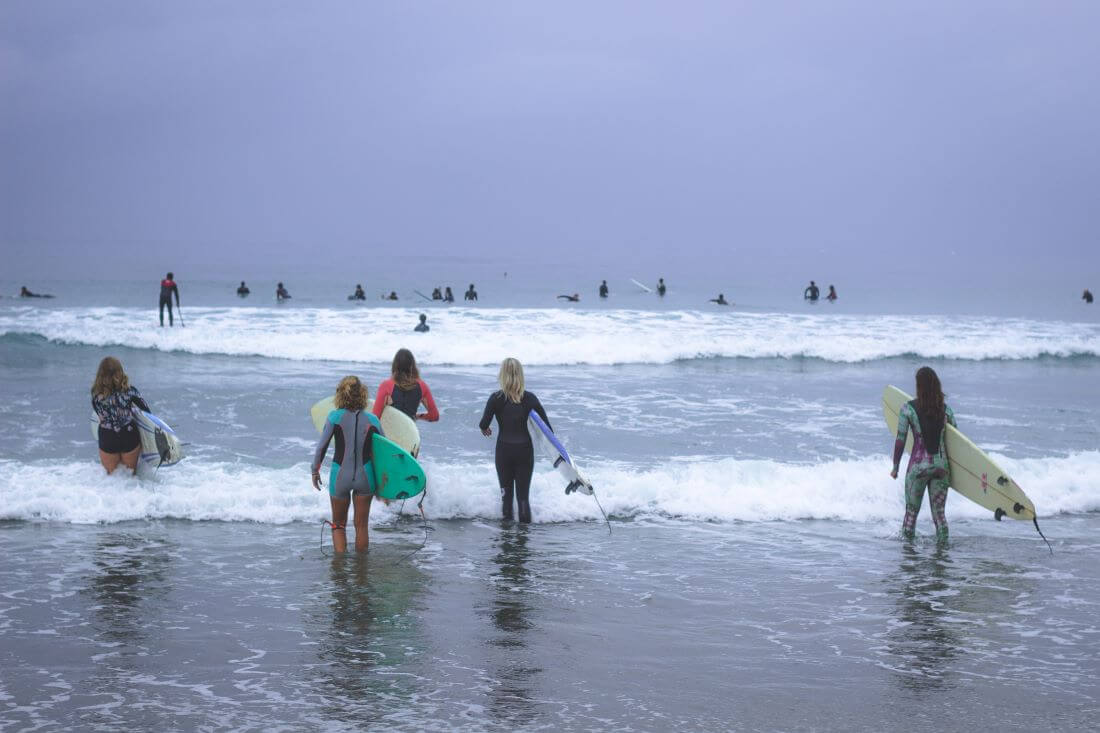 Women heading out into the ocean with their surfboards on an overcast day