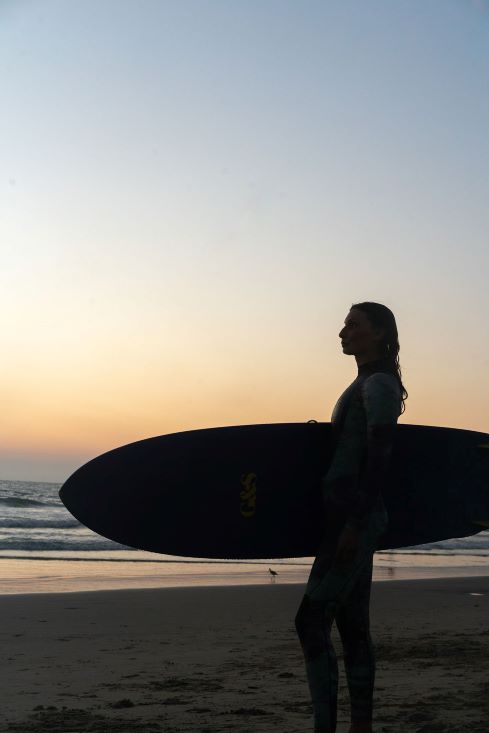 Profile silhouette of a woman holding her surfboard standing on the beach