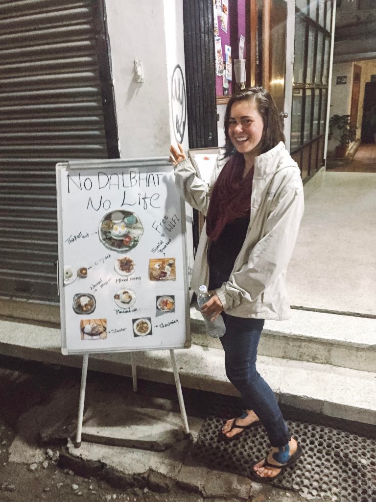 Sarah Bence standing next to a sign that says "no dal bhat no life"